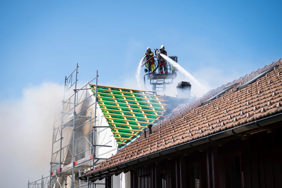 Zwei Feuerwehrmänner stehen auf einer Drehleiter und löschen einen Brand.